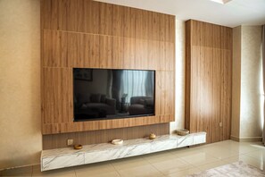 A modern living room with a large flat-screen TV mounted on a wooden panel wall, a marble console table below, and a tiled floor. - Vanilla Homes Luxury 2BR in Reem Island (Abu Dhabi)
