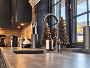 A modern kitchen with a stainless steel sink, a copper faucet, and decorative tree-shaped containers. - Modern Alpine Living in Ustaoset (Hol)