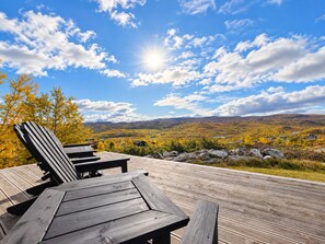 A wooden deck with a table and chairs, overlooking a scenic landscape with hills and autumn foliage. - Modern Alpine Living in Ustaoset (Hol)