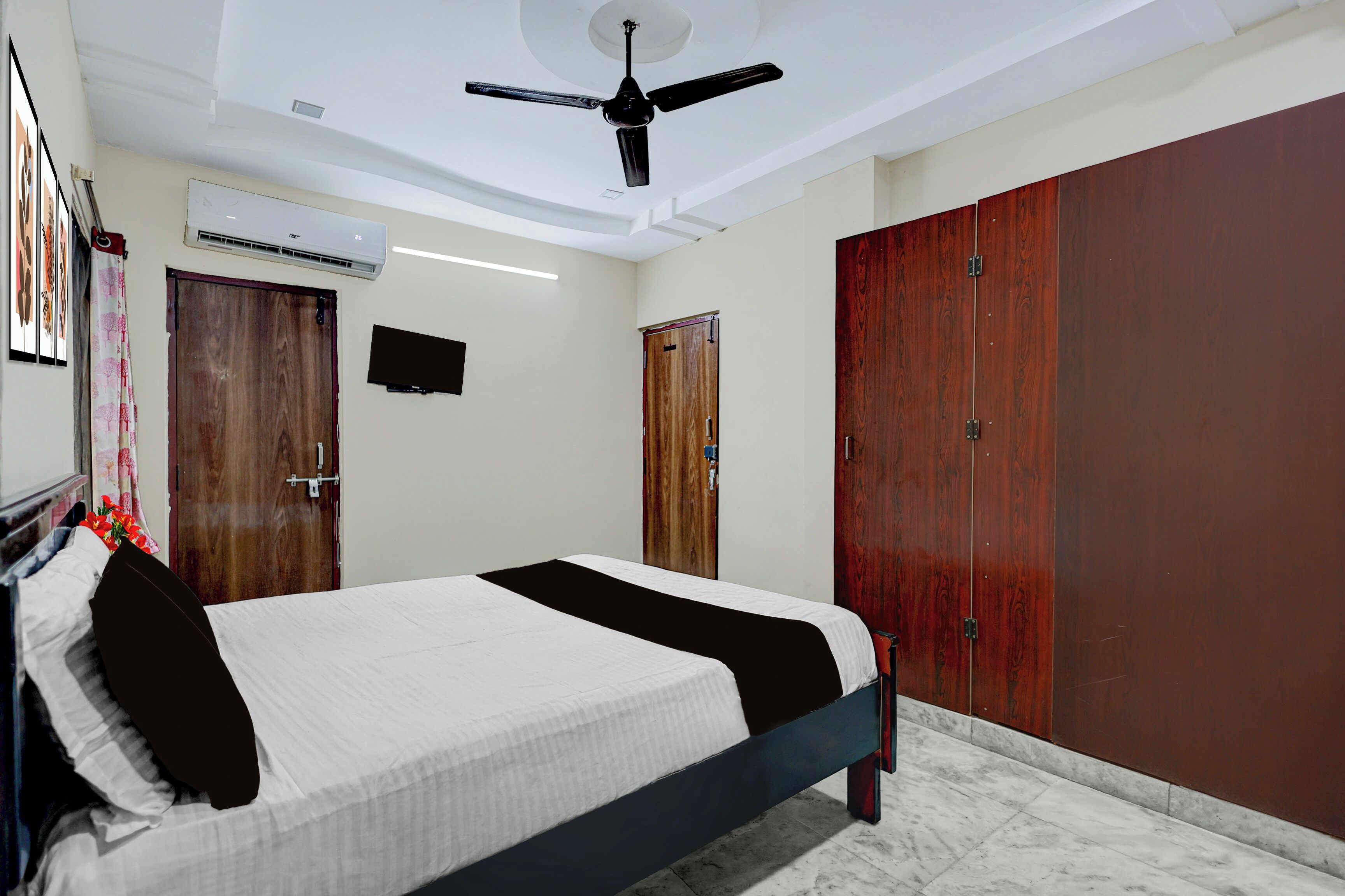 A bedroom with a bed, a ceiling fan, a TV, and wooden wardrobes.