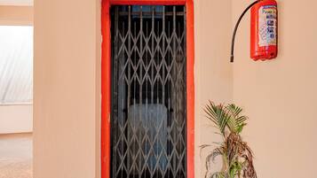 Una ventana con barrotes de metal, un extintor en la pared y una planta en maceta al lado de la ventana.