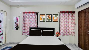 Une chambre à coucher comprenant un lit, des rideaux, un climatiseur fixé au mur et des œuvres d’art encadrées.