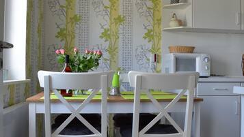 Ein Essbereich mit zwei weißen Stühlen, einem Tisch mit Blumenvase und einer Mikrowelle auf der Arbeitsfläche.