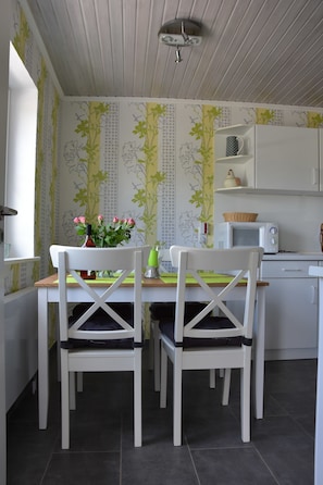 Un comedor con dos sillas blancas, una mesa con un florero y un microondas en la encimera.