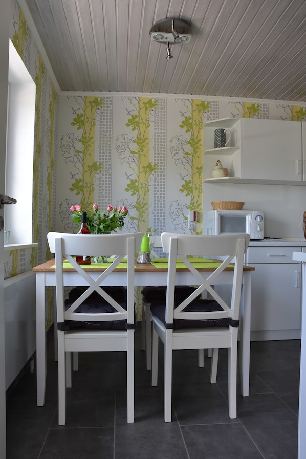 A dining area with two white chairs, a table with a vase of flowers, and a microwave on the counter.
