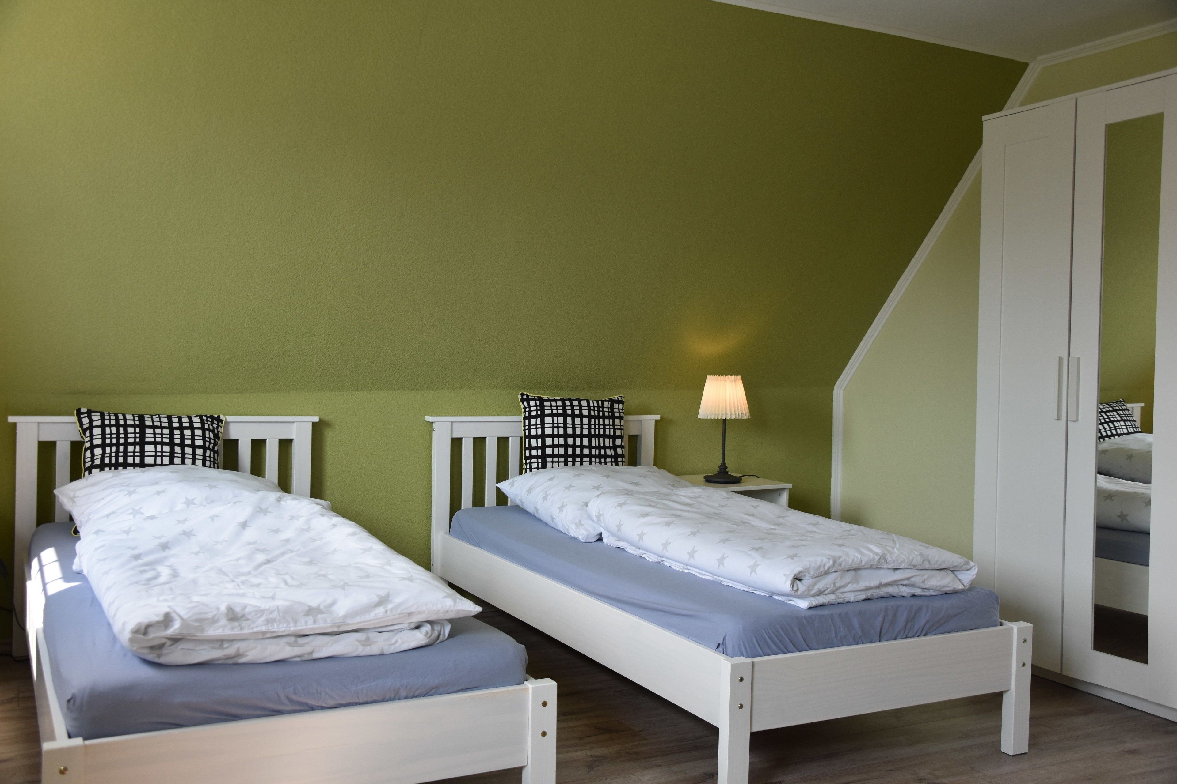 Una habitación con dos camas individuales, una mesita de noche con lámpara y un armario.