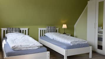 Una habitación con dos camas individuales, una mesita de noche con lámpara y un armario.