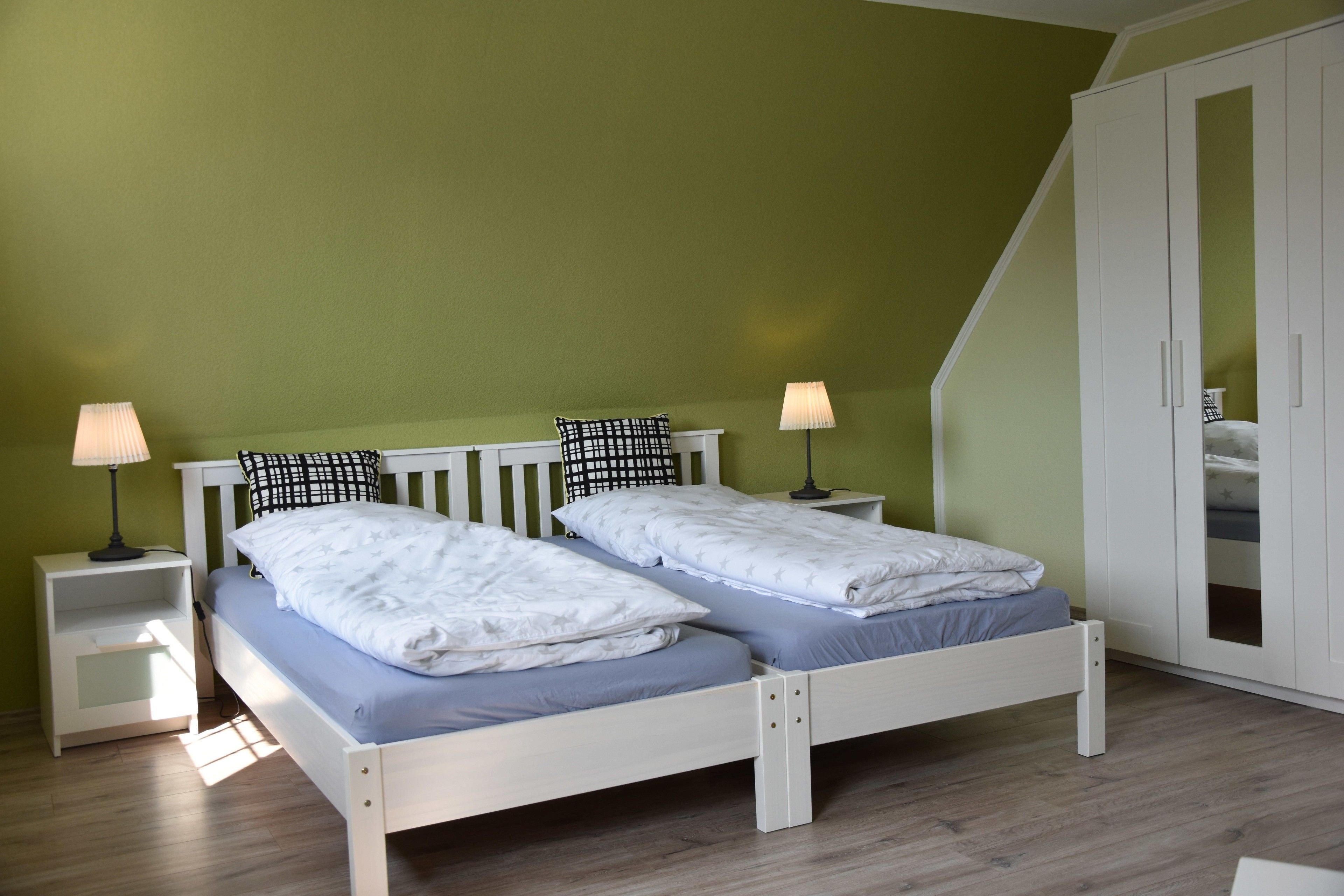 Ein Doppelbett mit Kopfteil, zwei Nachttische inklusive Lampen und ein Kleiderschrank mit Spiegel.
