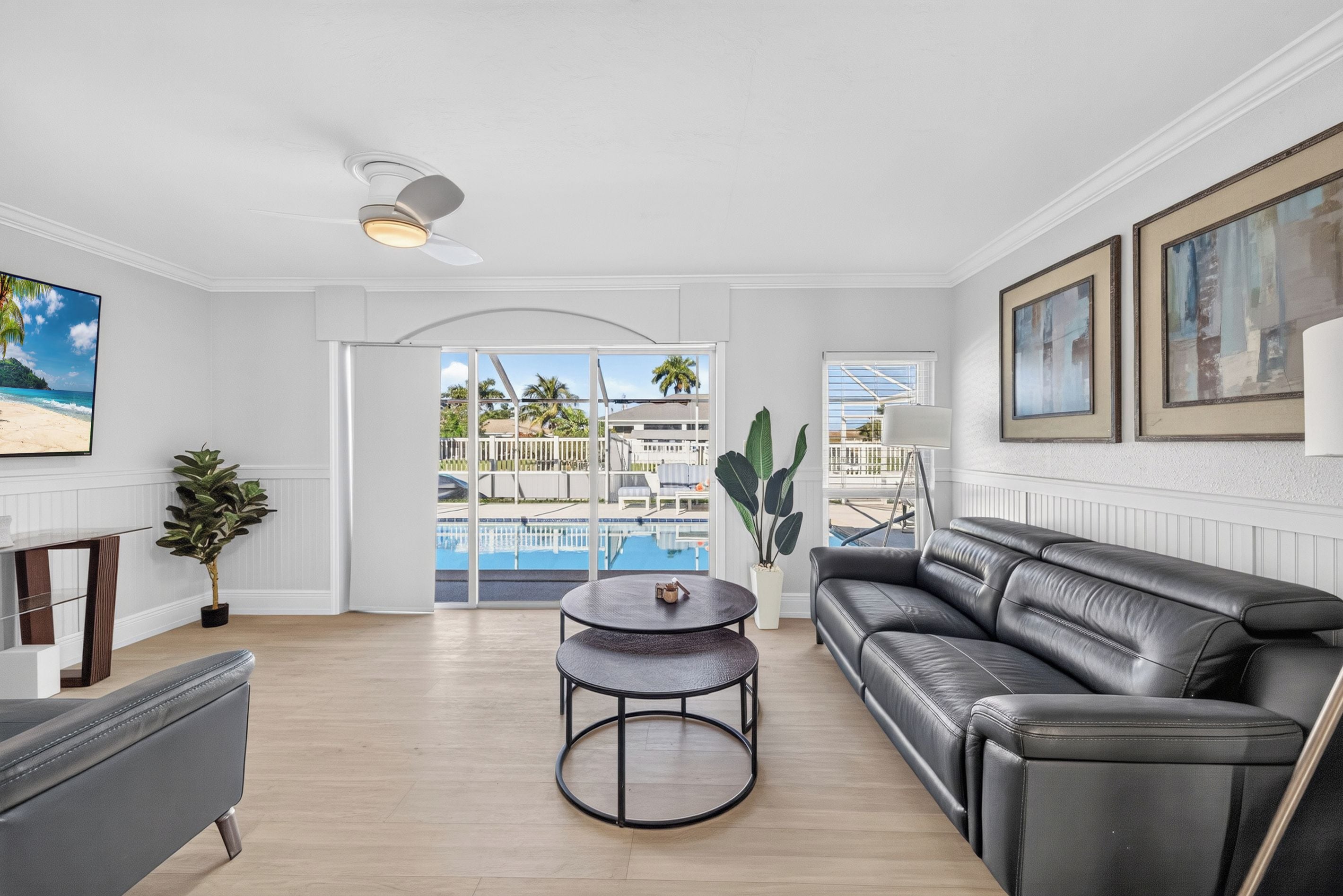 A modern living room with a leather sofa, a round coffee table, and a view of a pool and outdoor area.