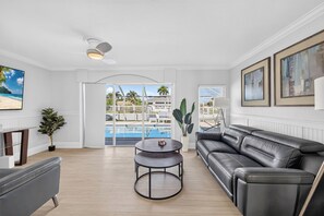 A modern living room with a leather sofa, a round coffee table, and a view of a pool and outdoor area. - Pool, Hot Tub & Water Access | Cape Coral Home (Cape Coral)