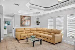 A modern living room with a sectional sofa, a glass coffee table, and a painting on the wall. - Pool, Hot Tub & Water Access | Cape Coral Home (Cape Coral)