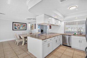 A modern kitchen with white cabinetry, a marble countertop, and a built-in dishwasher. - Pool, Hot Tub & Water Access | Cape Coral Home (Cape Coral)