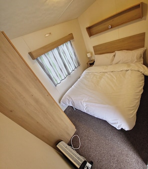 Quarto com cama, mesa de cabeceira, janela com cortinas e aquecedor no chão.