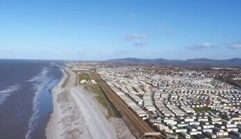 Una zona costera con numerosos edificios blancos alineados, probablemente un complejo residencial o comercial, con una playa y el océano a la izquierda.