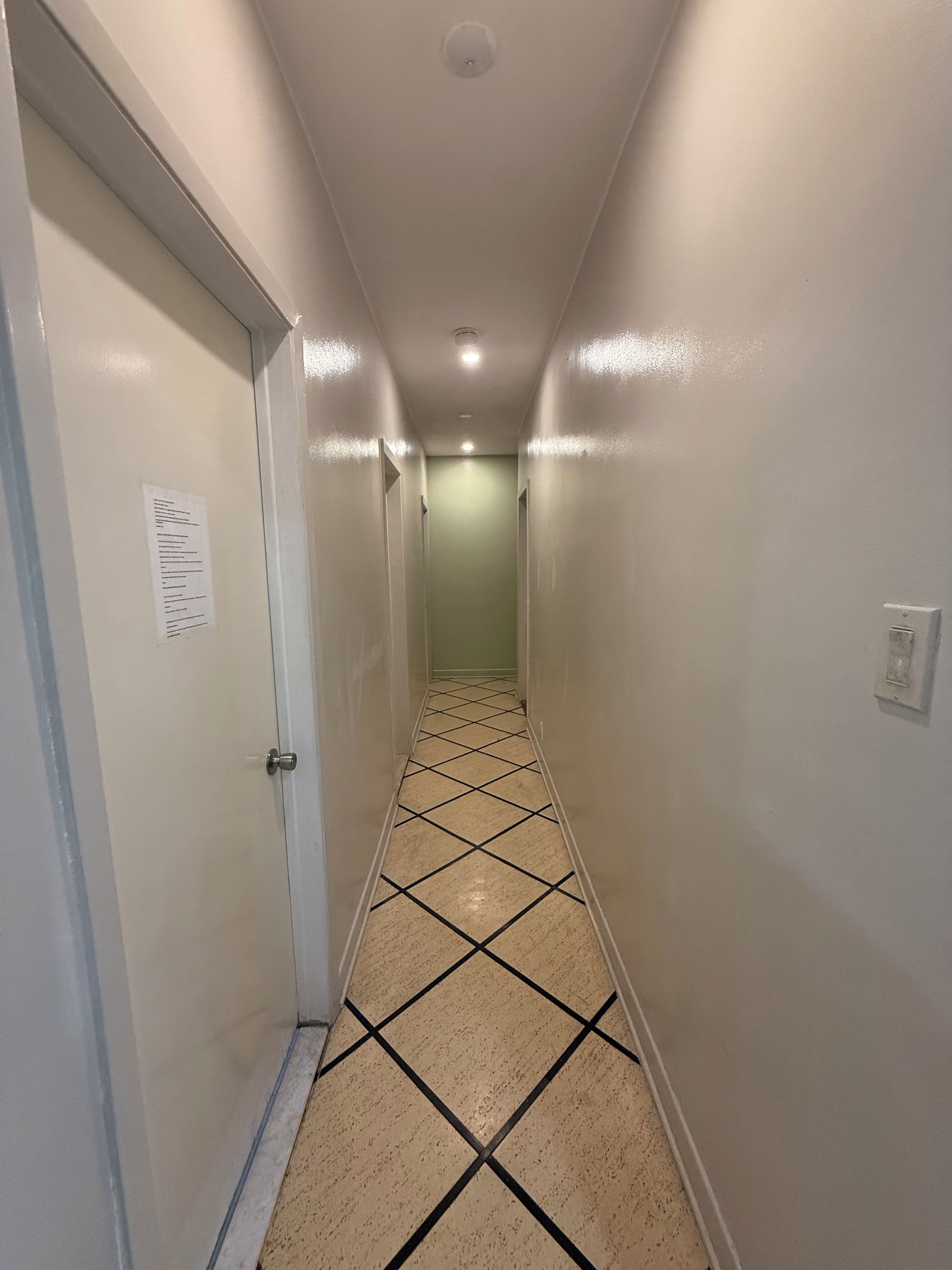A narrow hallway with a tiled floor, white walls, and a door on the left.
