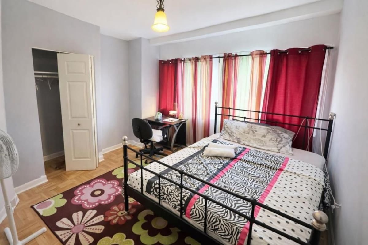 A bedroom with a bed, a desk, a chair, a wardrobe, and a fan.