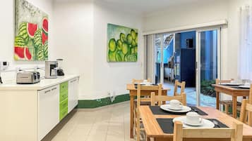 A modern kitchen with a dining area, featuring a coffee maker, toaster, and a painting of watermelons.