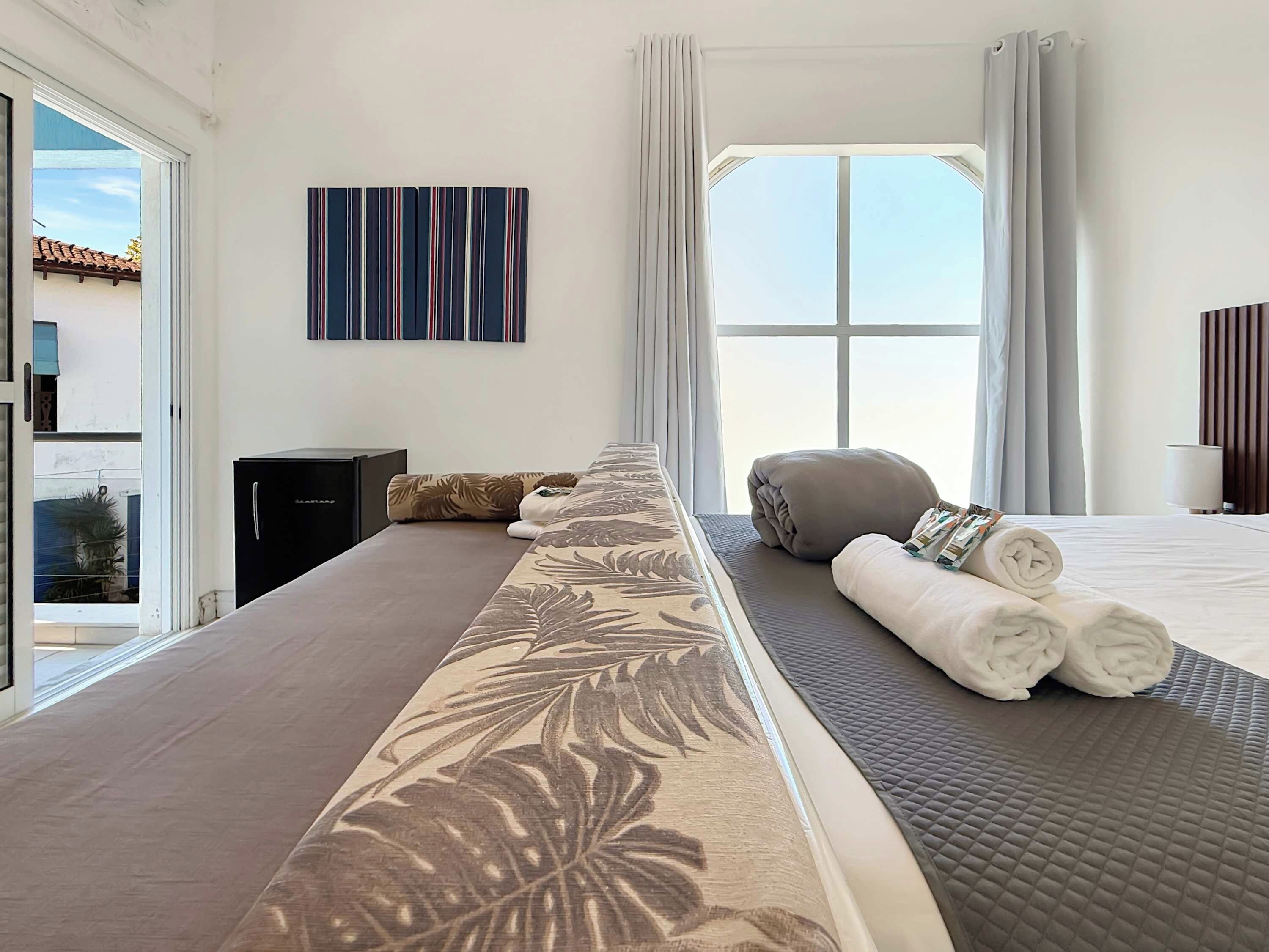 Une chambre d’hôtel avec un grand lit, une vue sur le ciel, un tableau au mur et une fenêtre avec des rideaux.