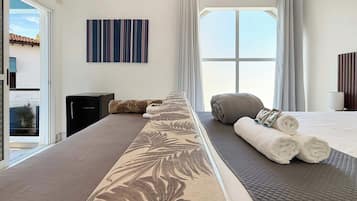 A hotel room with a large bed, a view of the sky, a painting on the wall, and a window with curtains.