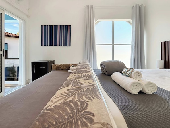 Une chambre d’hôtel avec un grand lit, une vue sur le ciel, un tableau au mur et une fenêtre avec des rideaux.