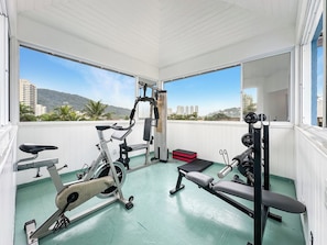 Une salle de sport équipée de matériel d’exercice, dotée de grandes fenêtres et offrant une vue sur les bâtiments et les collines.