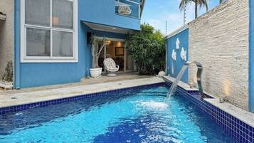 A swimming pool with a water feature, a chair, and a potted plant.