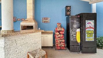An outdoor patio with a brick fireplace, a wooden bench, and a refrigerator with a beer advertisement.