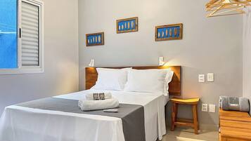 Een keurig opgeruimde hotelkamer met een bed, nachtkastjes, een klein houten krukje en een kledingrek.