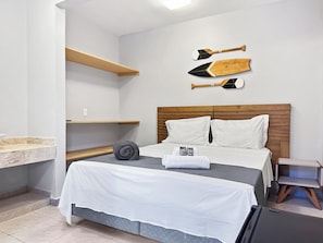 Une chambre d’hôtel avec un lit, une tête de lit en bois, une étagère fixée au mur et une petite table de chevet.