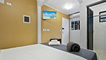 Quarto de hotel com cama, quadro de uma praia, porta e janela com persianas.