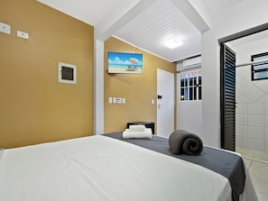 Habitación de hotel con cama, un cuadro de una playa, una puerta y una ventana con persianas.