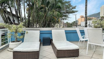 A rooftop terrace with two lounge chairs, a small table, and a potted plant.