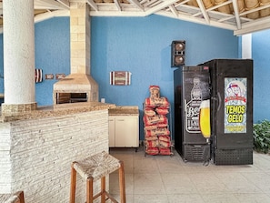 Une terrasse extérieure avec une cheminée en briques, un banc en bois et un réfrigérateur orné d’une publicité pour de la bière.