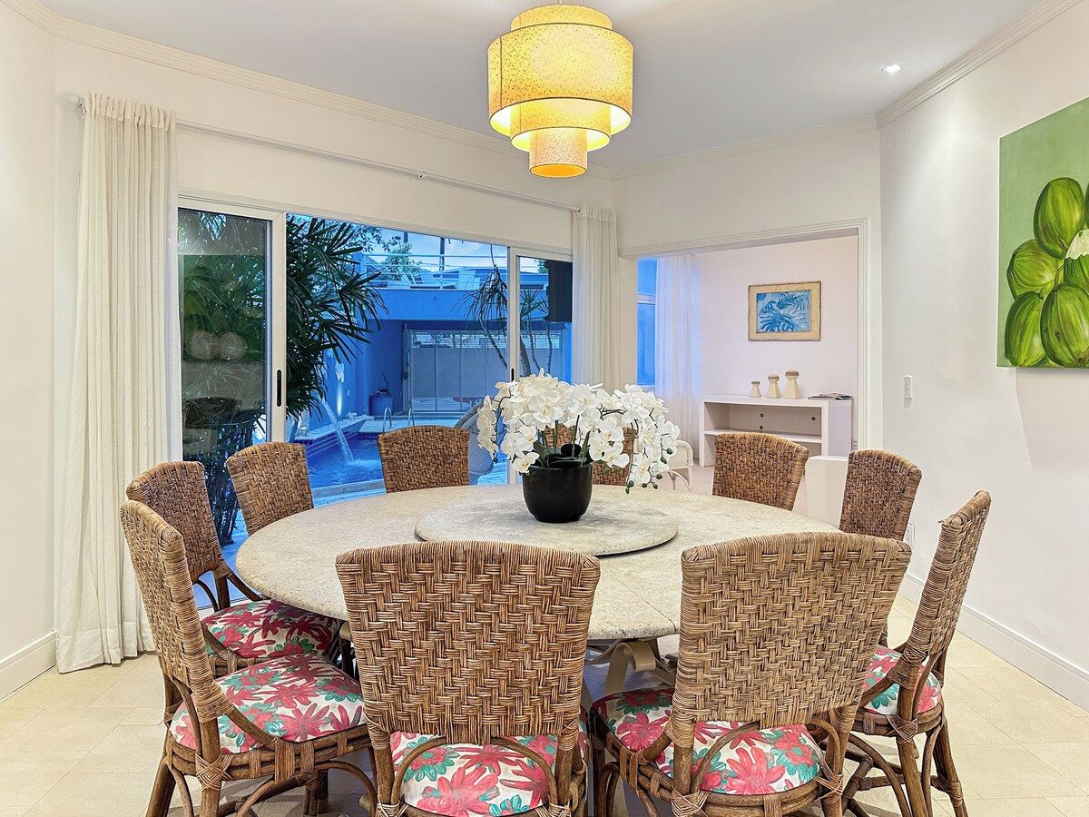 A dining area with a round table, wicker chairs, and a vase of white flowers.