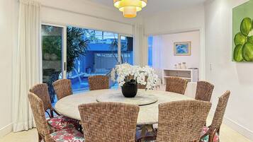 A dining area with a round table, wicker chairs, and a vase of white flowers.