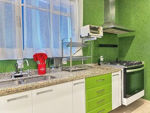 A kitchen with a gas stove, oven, and a microwave on the countertop. - Maraka_12 · Pousada Maraka , Quarto 12 (Guarujá)