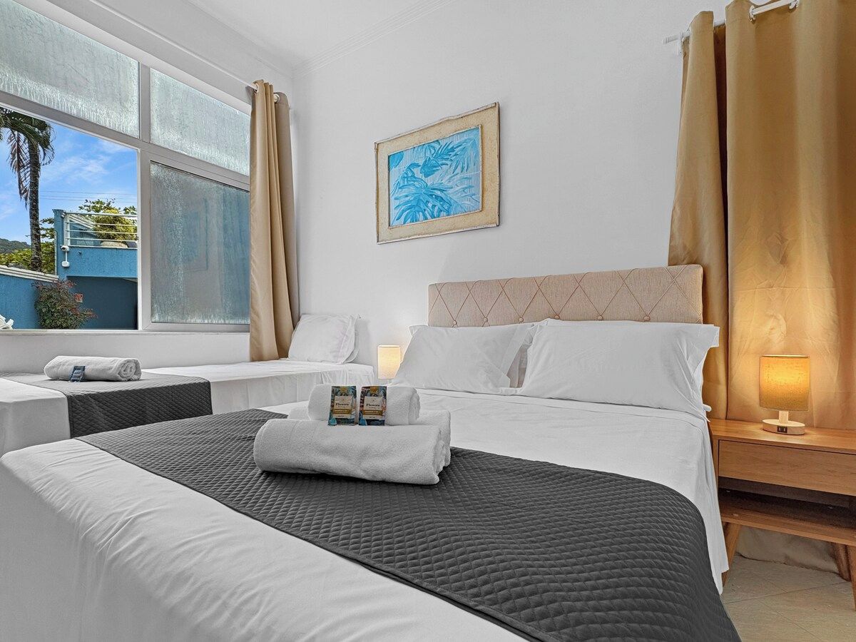 A hotel room with a bed, two bedside tables, a window with curtains, a wall-mounted picture, and a bedside lamp.