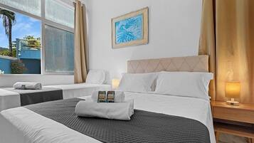 A hotel room with a bed, two bedside tables, a window with curtains, a wall-mounted picture, and a bedside lamp.