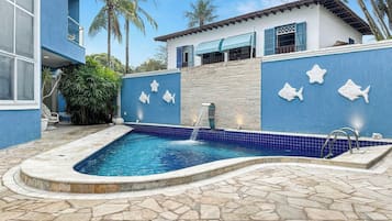 A swimming pool with a stone deck, surrounded by a blue wall with fish decorations, and a building with a balcony.
