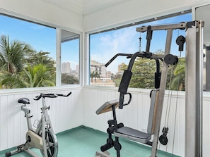A gym with exercise equipment, a stationary bike, and a view of palm trees and buildings through large windows.