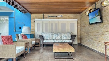 A room with a sofa, chairs, a coffee table, a television, and a wall-mounted lamp.