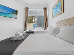 A hotel room with a bed, a window with curtains, a painting, and a view of the beach.