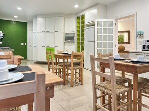 A modern kitchen with white cabinets, a green accent wall, and a dining area with wooden furniture.