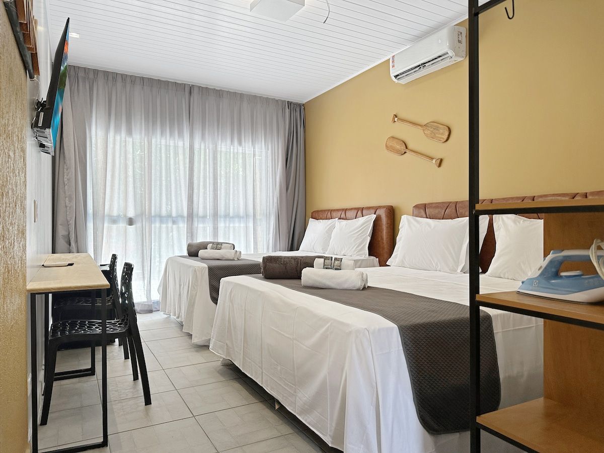 A hotel room with two beds, a desk, a chair, and a dining table.