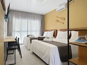 A hotel room with two beds, a desk, a chair, and a dining table.