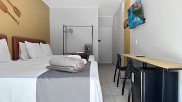 A hotel room with a bed, a desk, a chair, a TV, and an air conditioning unit.