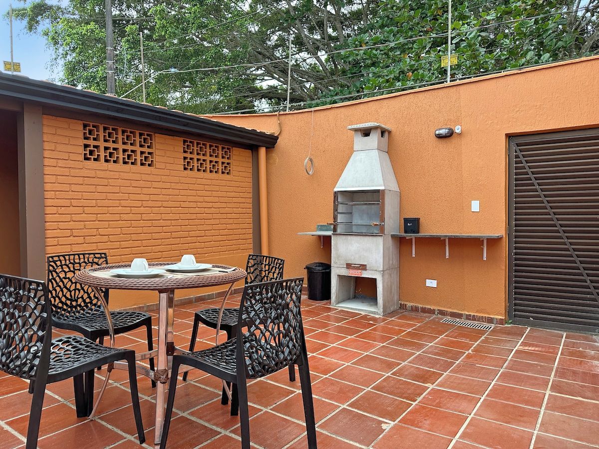 An outdoor patio with a brick wall, a grill, and metal chairs.