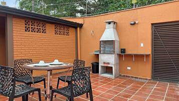 An outdoor patio with a brick wall, a grill, and metal chairs.