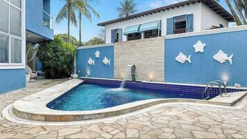 Piscina com deck de pedra, cercada por uma parede azul com decorações de peixes, e um edifício com varanda.