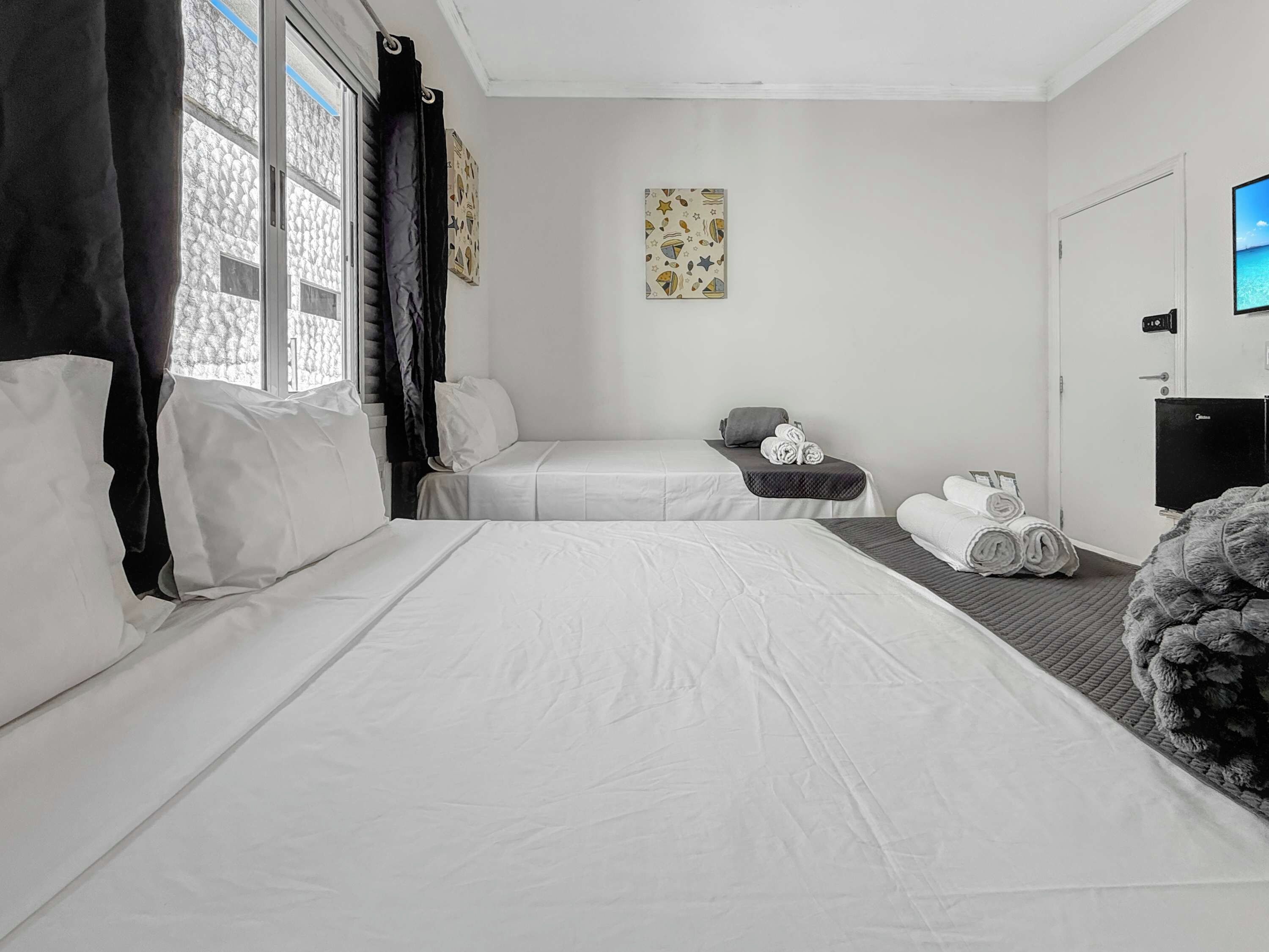 Quarto de hotel com duas camas, televisão de tela plana e janela com cortinas.
